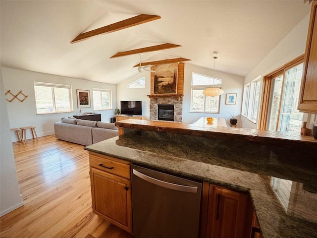 kitchen featuring pendant lighting, lofted ceiling, light hardwood / wood-style floors, a stone fireplace, and stainless steel dishwasher