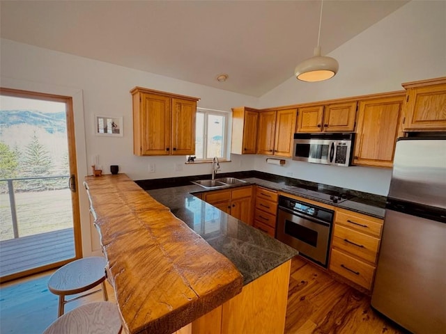 kitchen featuring appliances with stainless steel finishes, lofted ceiling, sink, kitchen peninsula, and light hardwood / wood-style flooring