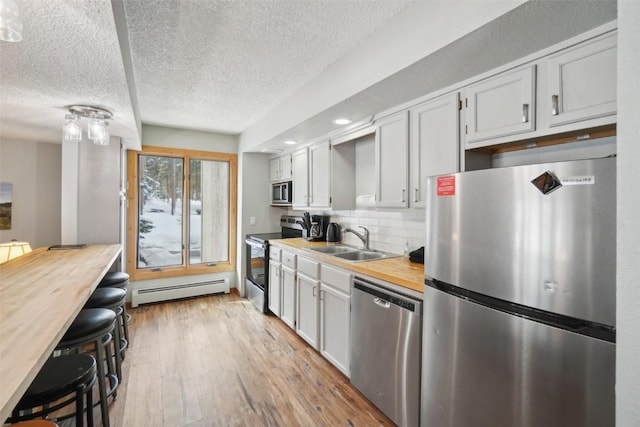 kitchen featuring stainless steel appliances, a baseboard radiator, light wood-style flooring, a sink, and butcher block countertops