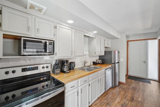 kitchen with stainless steel appliances, a sink, visible vents, backsplash, and light wood finished floors