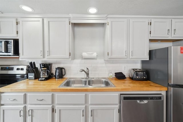 kitchen featuring stainless steel appliances, tasteful backsplash, wooden counters, white cabinetry, and a sink