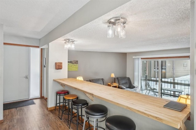 kitchen with a textured ceiling, butcher block counters, wood finished floors, and baseboards