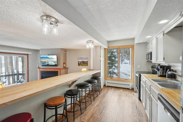 kitchen with appliances with stainless steel finishes, a kitchen breakfast bar, baseboard heating, light wood-style floors, and a sink