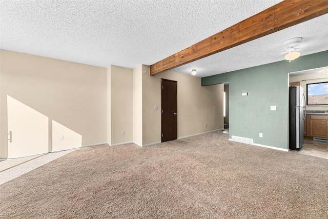 empty room featuring beam ceiling, visible vents, light carpet, a textured ceiling, and baseboards