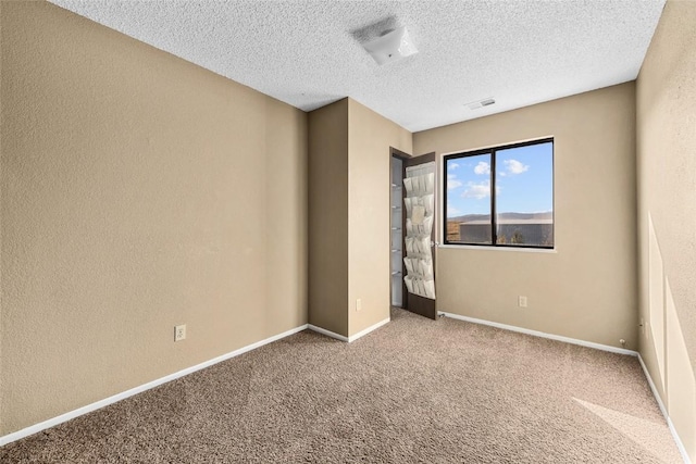 unfurnished bedroom featuring a textured ceiling, a textured wall, carpet flooring, visible vents, and baseboards