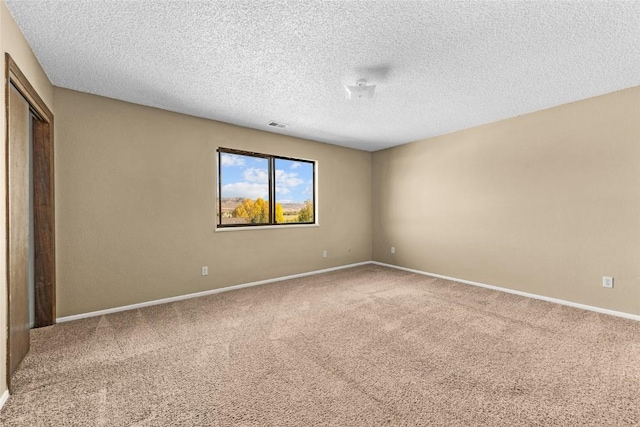 spare room with visible vents, a textured ceiling, baseboards, and carpet flooring