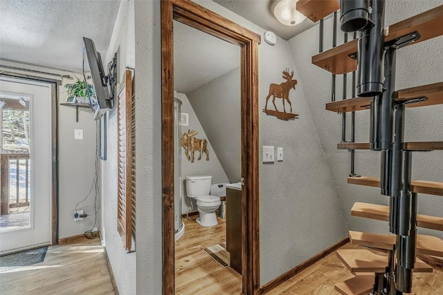 corridor with a textured wall, a textured ceiling, baseboards, and wood finished floors