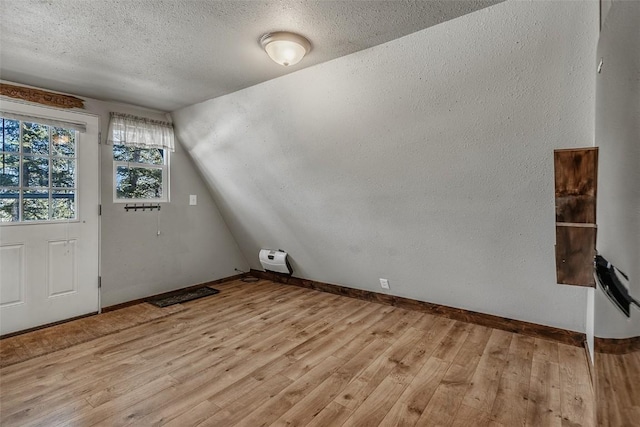 bonus room with lofted ceiling, light wood-style floors, baseboards, and a textured ceiling