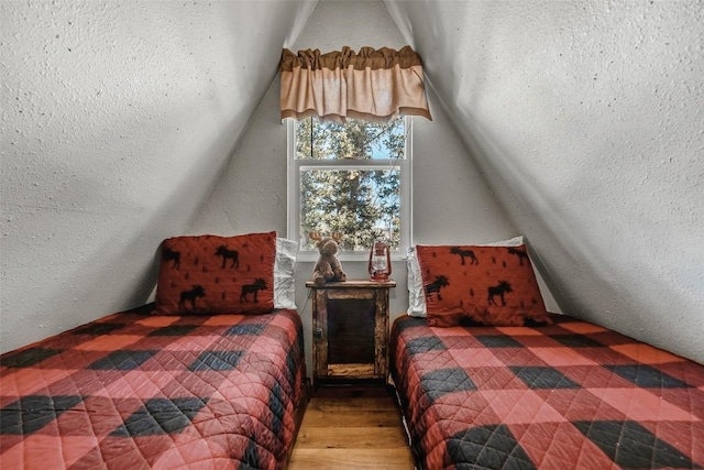 bedroom featuring vaulted ceiling, wood finished floors, and a textured wall