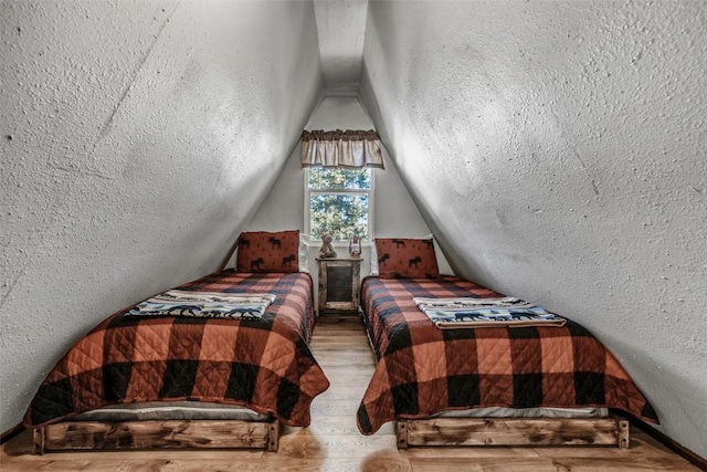 bedroom with vaulted ceiling, a textured wall, and wood finished floors