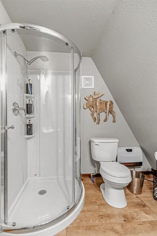 full bath featuring lofted ceiling, a shower stall, toilet, and wood finished floors