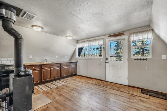 kitchen with vaulted ceiling, a textured ceiling, a wood stove, and light wood-style floors