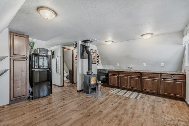 kitchen featuring light wood-style floors, a wood stove, a sink, a textured ceiling, and black appliances