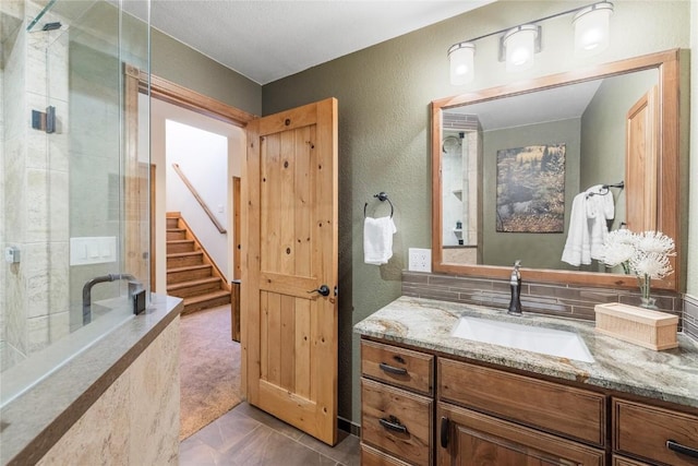 bathroom with a textured wall, a shower stall, a closet, and vanity