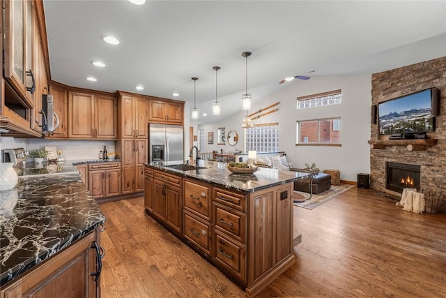 kitchen with appliances with stainless steel finishes, brown cabinets, decorative light fixtures, a kitchen island with sink, and a sink