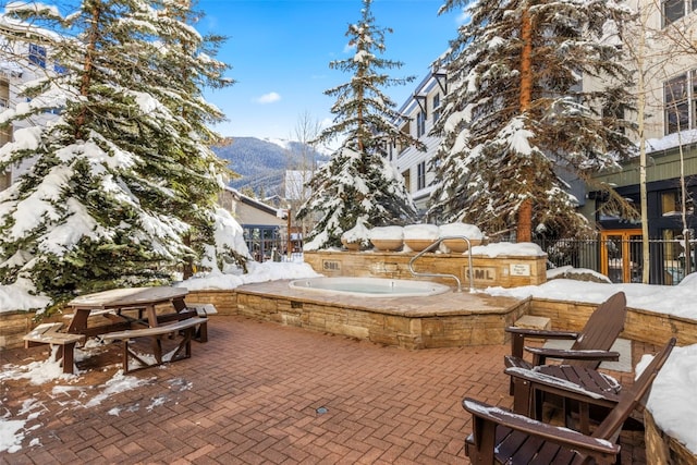 snow covered patio featuring an in ground hot tub, grilling area, fence, and a mountain view