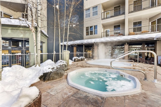 snow covered pool featuring a patio and an in ground hot tub