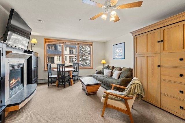 living area with a ceiling fan, a glass covered fireplace, and light colored carpet