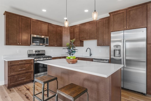 kitchen featuring appliances with stainless steel finishes, light wood-type flooring, hanging light fixtures, and sink