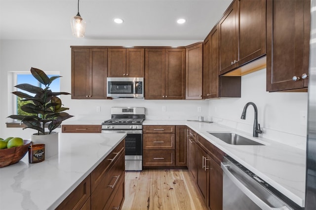 kitchen with sink, decorative light fixtures, light hardwood / wood-style floors, light stone counters, and stainless steel appliances