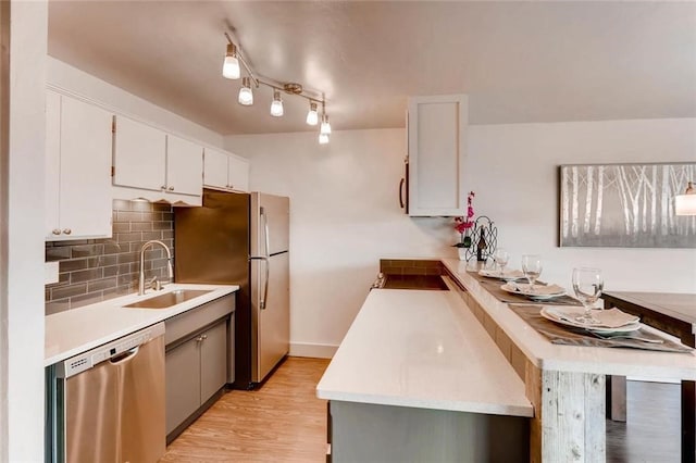 kitchen with sink, white cabinetry, tasteful backsplash, light hardwood / wood-style flooring, and stainless steel dishwasher