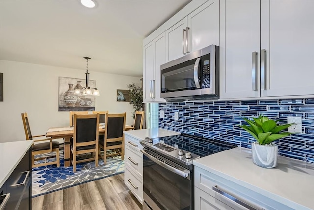 kitchen with decorative backsplash, white cabinetry, appliances with stainless steel finishes, and hanging light fixtures