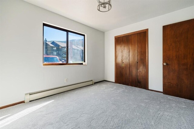 unfurnished bedroom with light carpet, a closet, and a baseboard heating unit