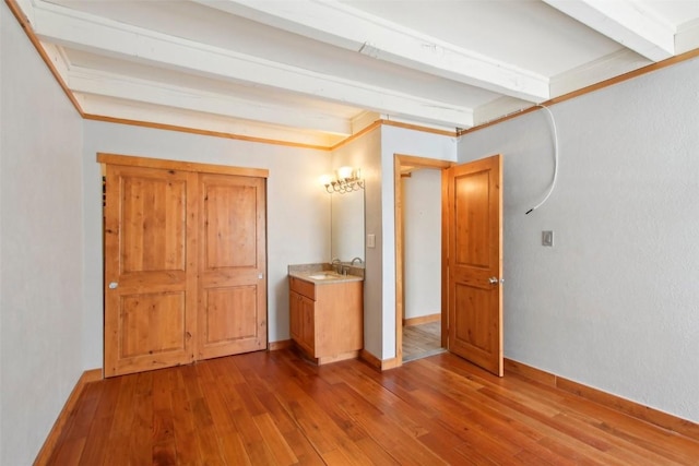 unfurnished bedroom with hardwood / wood-style floors, beam ceiling, and sink