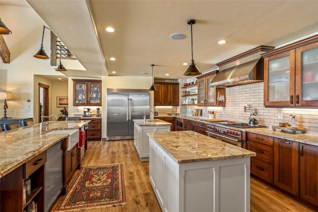 kitchen with white cabinetry, sink, high end appliances, a center island with sink, and wall chimney exhaust hood