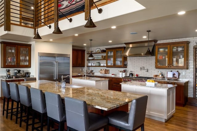 kitchen featuring a large island, sink, appliances with stainless steel finishes, extractor fan, and light stone countertops