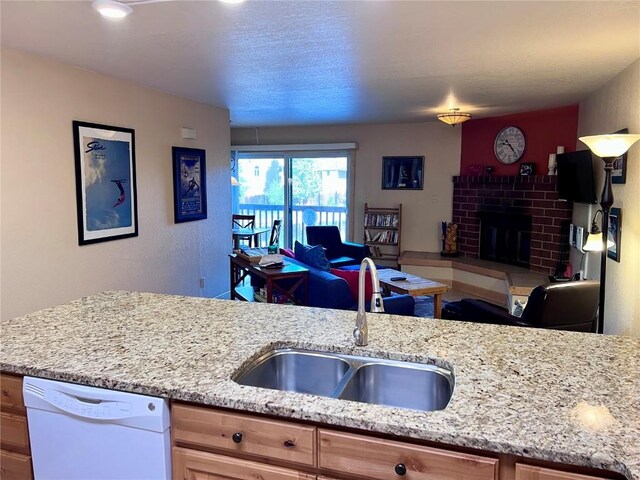 kitchen featuring white dishwasher, light stone countertops, sink, and a brick fireplace