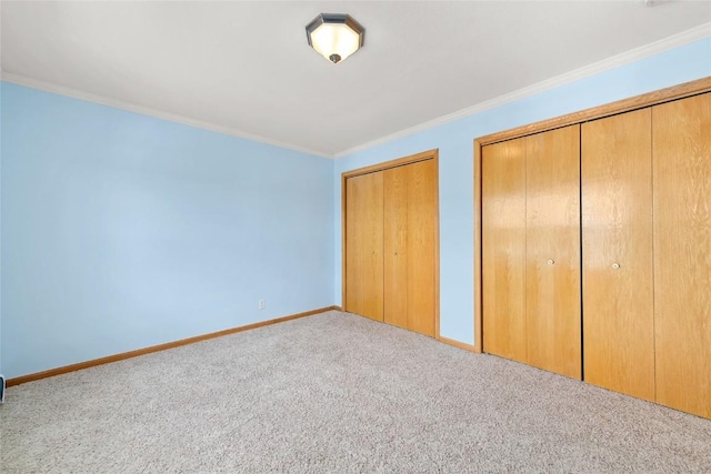 unfurnished bedroom featuring multiple closets, crown molding, and light colored carpet