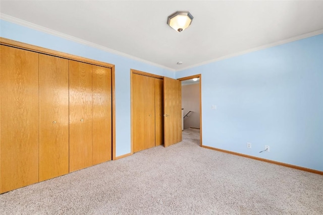 unfurnished bedroom featuring two closets, light colored carpet, and crown molding