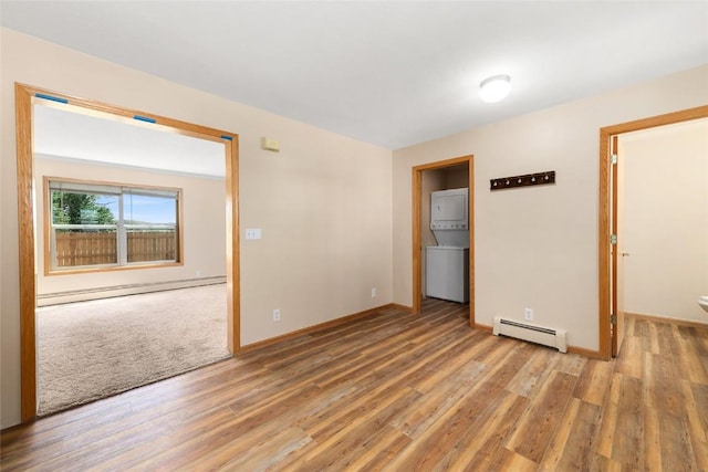 spare room with stacked washer / drying machine, light wood-type flooring, and baseboard heating