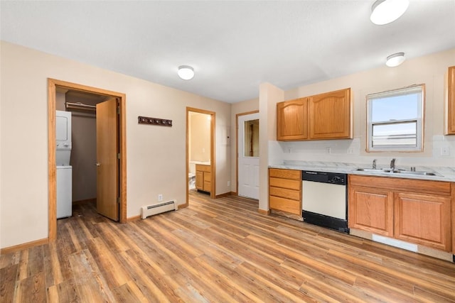 kitchen with sink, stacked washing maching and dryer, a baseboard radiator, white dishwasher, and light hardwood / wood-style floors