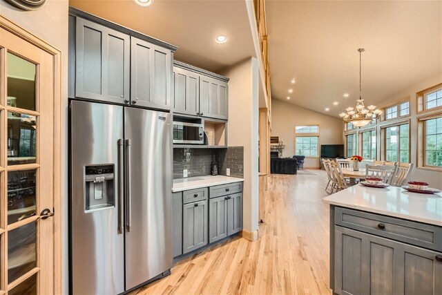 kitchen with pendant lighting, gray cabinets, tasteful backsplash, stainless steel fridge with ice dispenser, and a chandelier