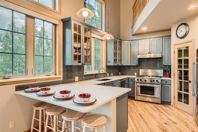 kitchen featuring gas range, hanging light fixtures, kitchen peninsula, a breakfast bar area, and gray cabinets