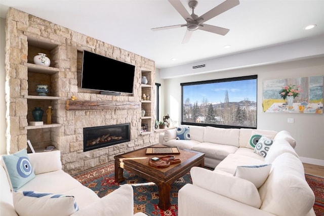 living room featuring ceiling fan, wood-type flooring, and a stone fireplace