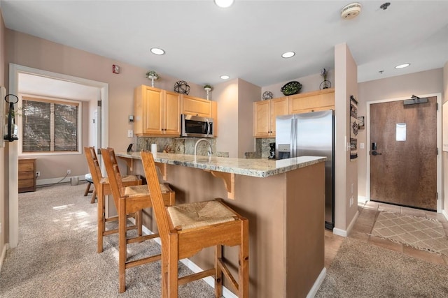 kitchen featuring light brown cabinetry, appliances with stainless steel finishes, decorative backsplash, and a breakfast bar