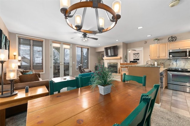 dining area featuring ceiling fan with notable chandelier, light tile patterned floors, and a tile fireplace