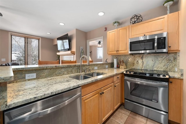 kitchen featuring stainless steel appliances, backsplash, light stone counters, and sink