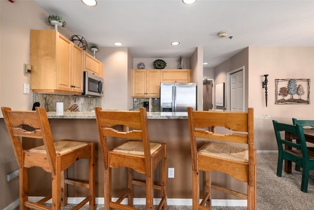 kitchen featuring appliances with stainless steel finishes, light brown cabinetry, carpet flooring, and backsplash