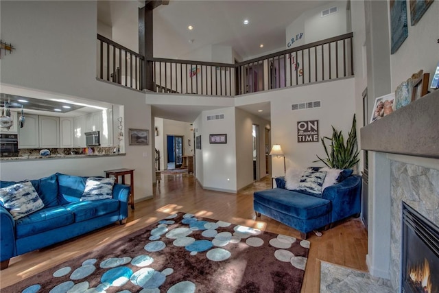 living room with light wood-type flooring, a tile fireplace, and a towering ceiling