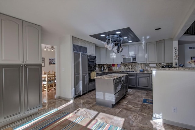 kitchen with light stone counters, backsplash, a kitchen island, gray cabinetry, and appliances with stainless steel finishes