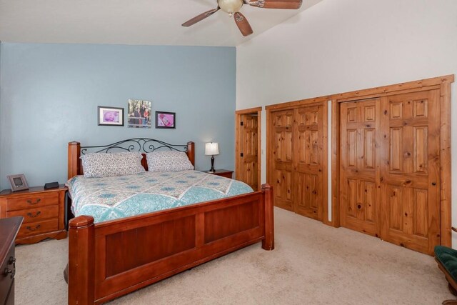 carpeted bedroom with two closets, ceiling fan, and vaulted ceiling