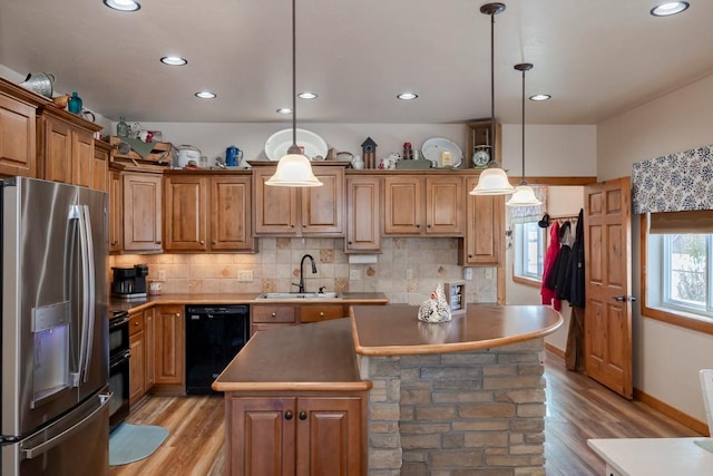 kitchen with black appliances, decorative light fixtures, a center island, and light hardwood / wood-style flooring