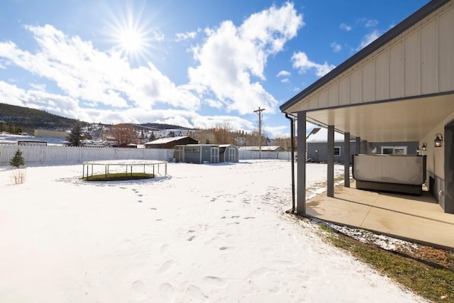 yard layered in snow featuring a storage shed and a trampoline