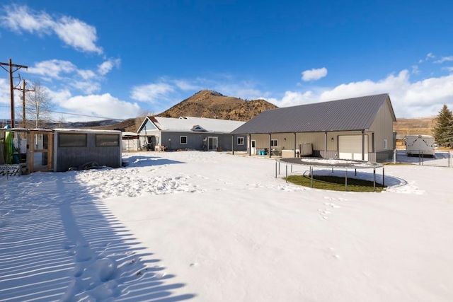 snow covered property featuring a mountain view, a trampoline, a garage, and an outdoor structure