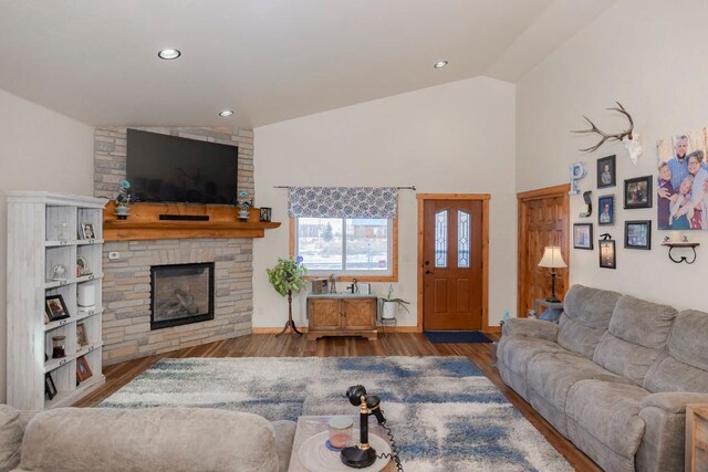 living room with hardwood / wood-style flooring, vaulted ceiling, and a stone fireplace