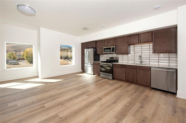 kitchen with decorative backsplash, light wood-type flooring, dark brown cabinetry, stainless steel appliances, and sink